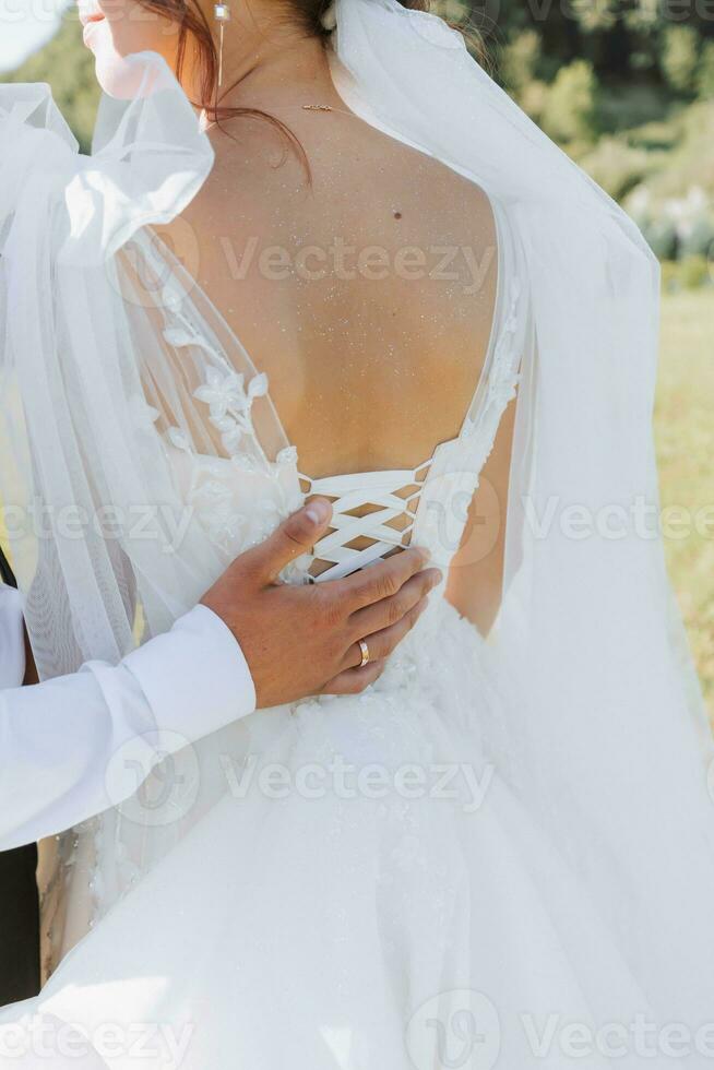 Wedding photo in nature. The bride's shoulders are open, the groom's hand is on the bride's shoulder. Beautiful hairstyle and hair decoration. Portrait of the bride and groom in the forest