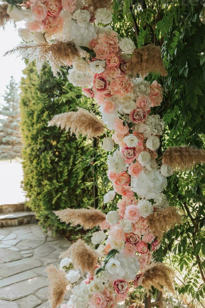 The wedding arch in the park is made of fresh flowers and dry reeds. Outdoor wedding ceremony in nature in a green corridor. White chairs for the ceremony photo