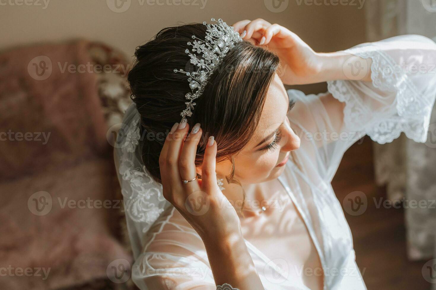 a beautiful bride in a white robe with an open bust and a crown on her head. The bride is preparing for the wedding. bride's fees the wedding day of the newlyweds. photo