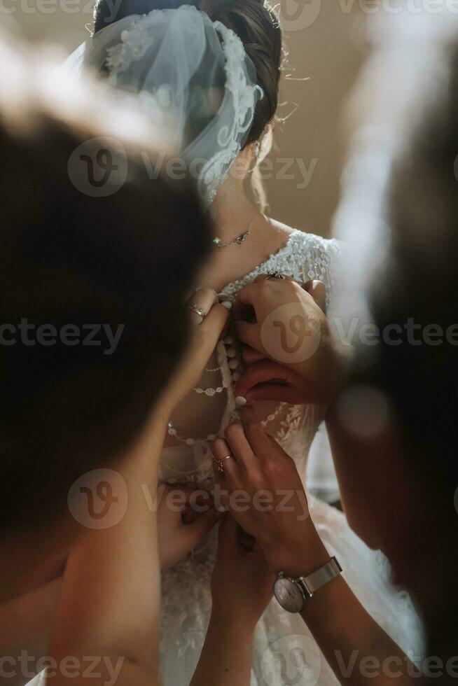 Portrait of the bride with her friends. The bride's friends fasten the bride's dress. Brunettes Open shoulders. photo