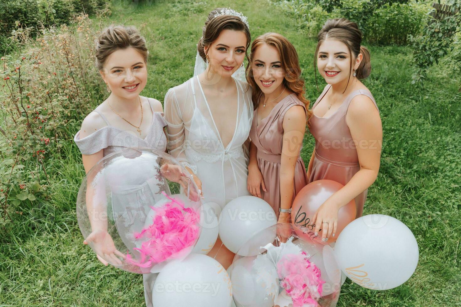 el damas de honor Mira a el sonriente novia. el novia y su divertido amigos celebrar un despedida de soltera fiesta al aire libre en pareo vestidos. el novia y amigos en el césped debajo el abierto cielo foto