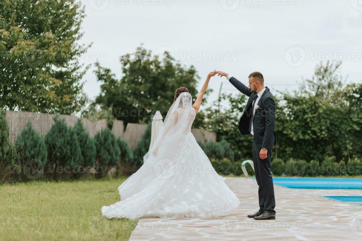 Portrait of the bride and groom. Bride and groom dancing by the pool, holding hands. Wedding walk near the hotel. Long train of the dress photo