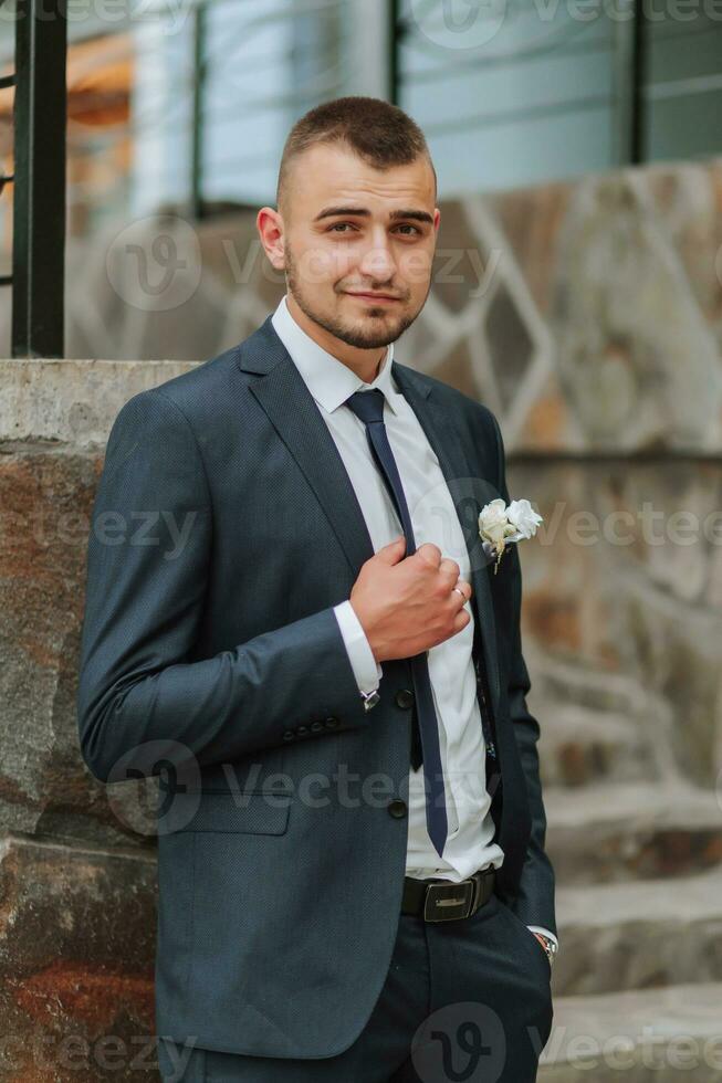 A man in a classic suit and white shirt poses near a stone wall. Men's style. Fashion. Business. photo