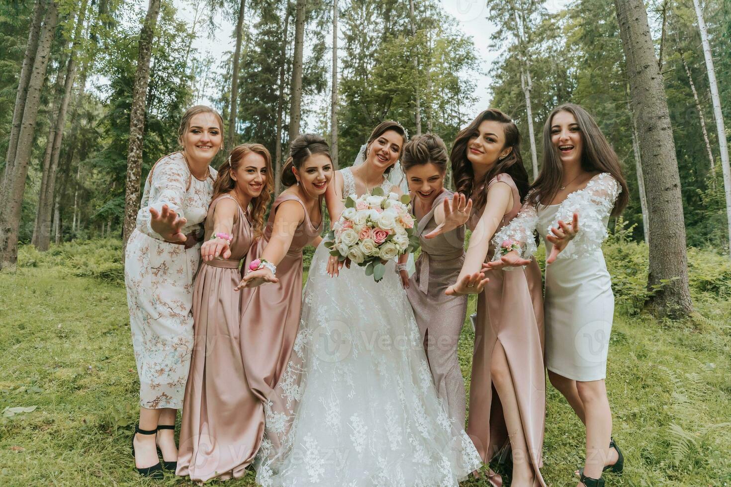 A group of beautiful girls with a bride in identical dresses are smiling, celebrating and having fun together against the background of nature and tall trees. Girls party photo