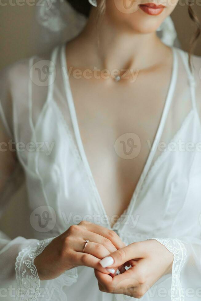 beautiful bride in a white robe with an open bust holding a diamond wedding ring The bride is preparing for the wedding. bride's fees the wedding day of the newlyweds. photo