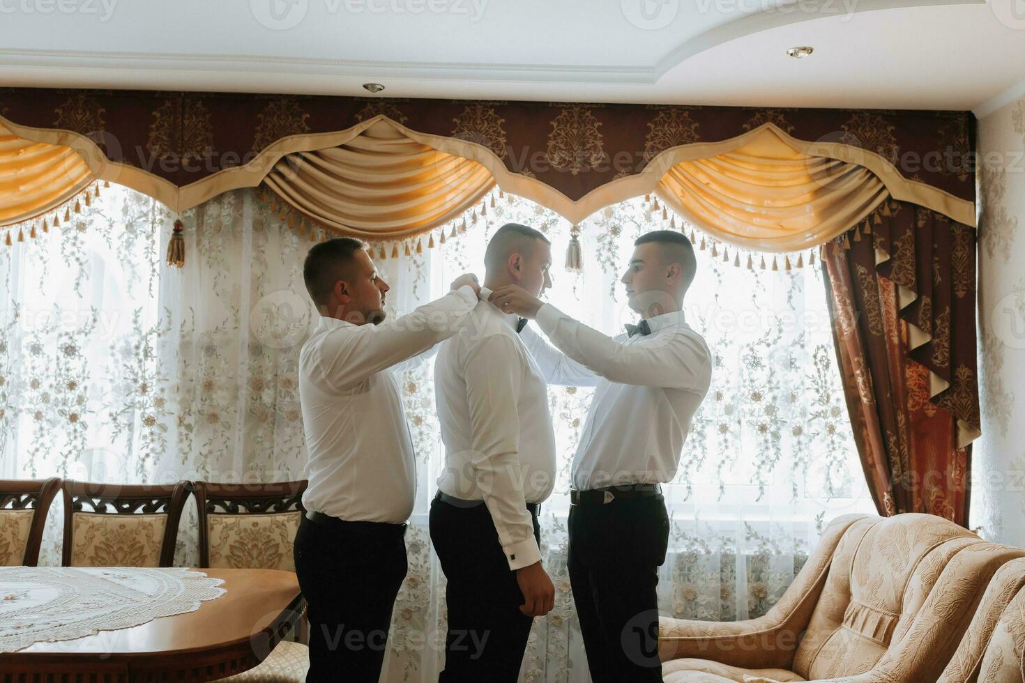 Wedding photography. Friends help the groom get dressed. Groom's morning. Style. Fashion. The same clothes photo