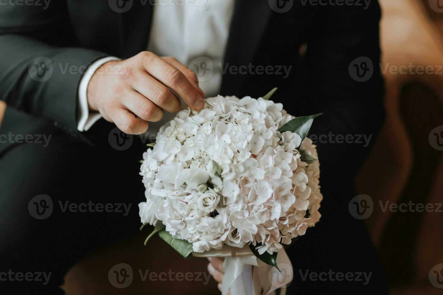 portrait. A man in a white shirt, a black suit is sitting, posing on a sofa, holding a bouquet. A stylish watch. Men's style. Fashion. Business photo
