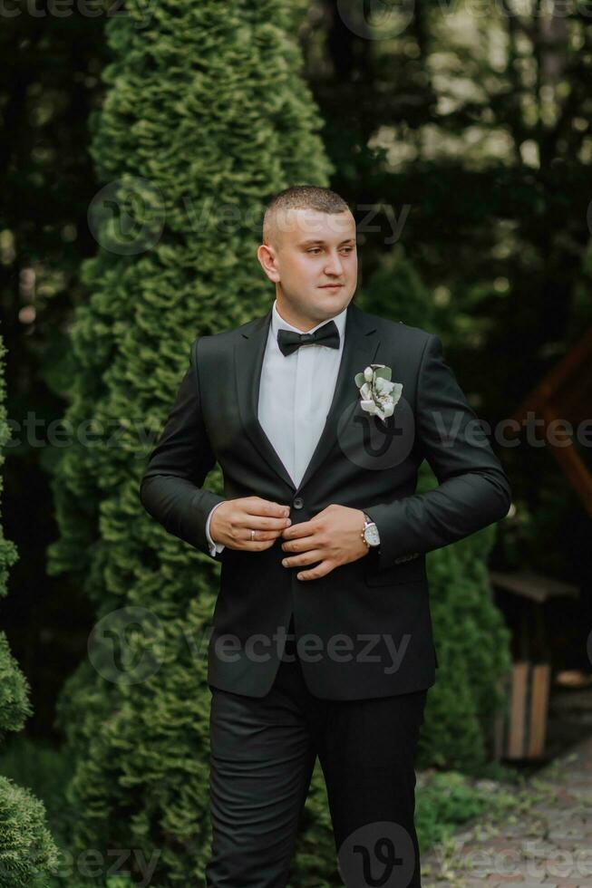 portrait of the groom in a classic suit against a background of green trees. A young man. Style. Fashion photo