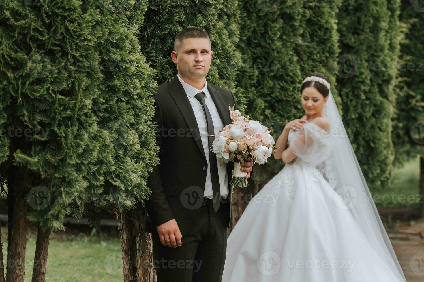the bride and groom pose against the background of green trees. Wedding walk in nature in the park photo