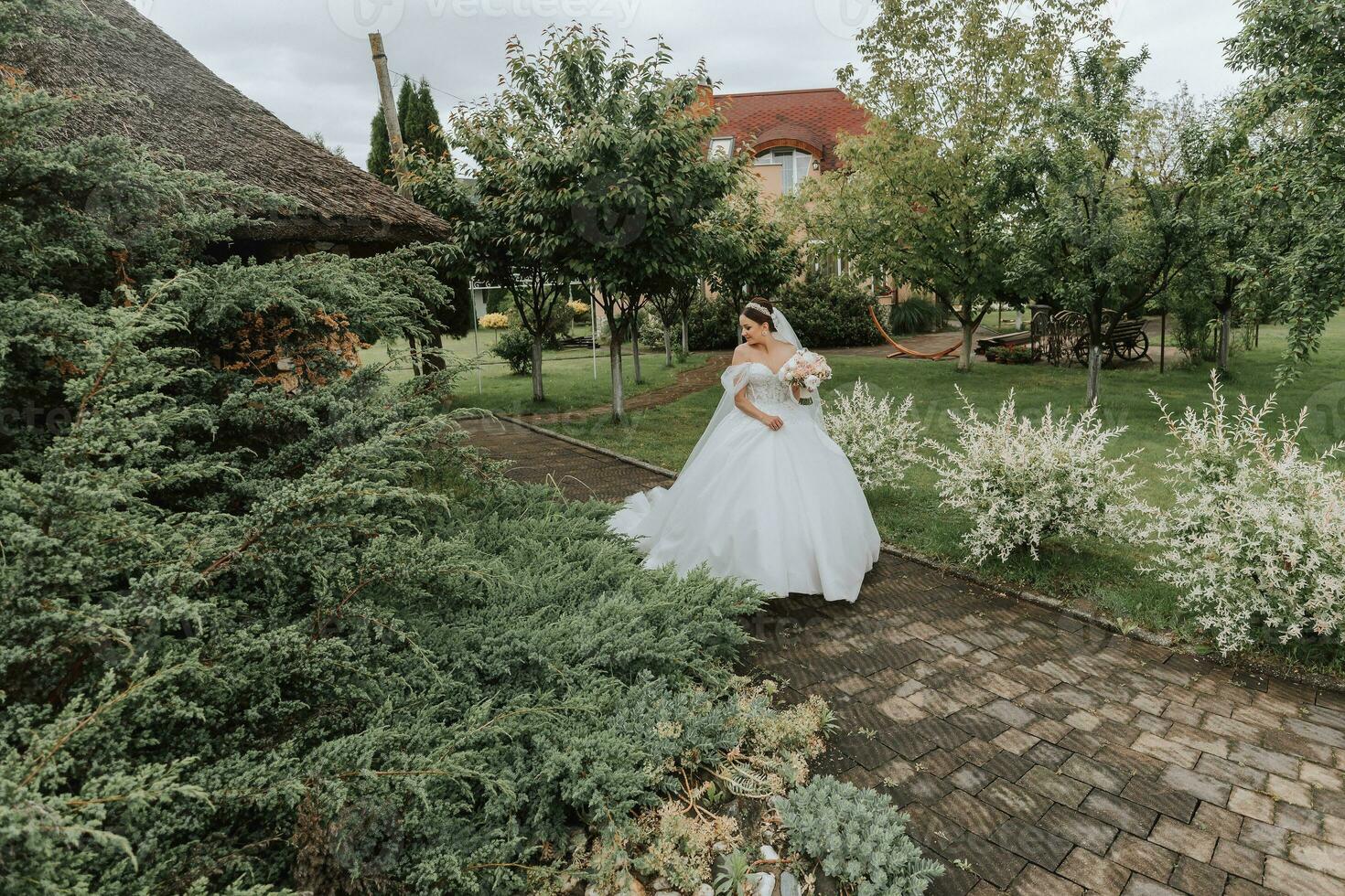 Portrait of a beautiful bride in a white wedding dress with a long train with a modern hairstyle and a veil walking in the garden. Wedding concept photo