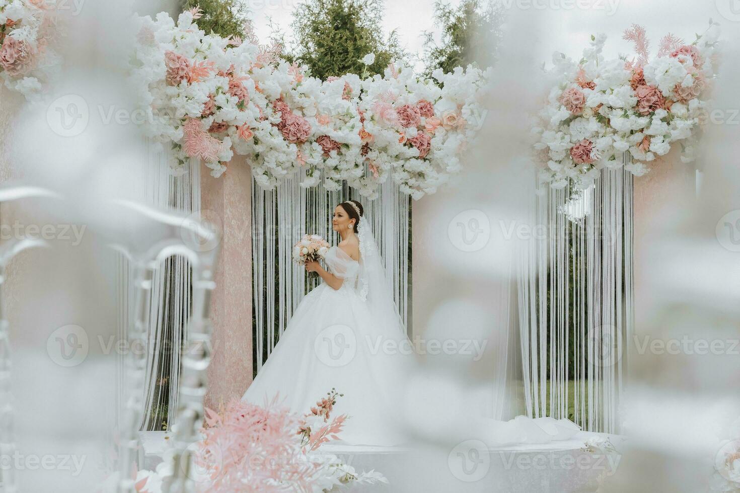Attractive bride at the ceremony on her wedding day with an arch made of pink and white flowers. Beautiful newlyweds, a young woman in a white dress with a long train, men in a black suit. photo