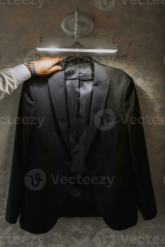 a man's jacket hangs on a hanger, a businessman man takes it in his hands and prepares for a meeting photo