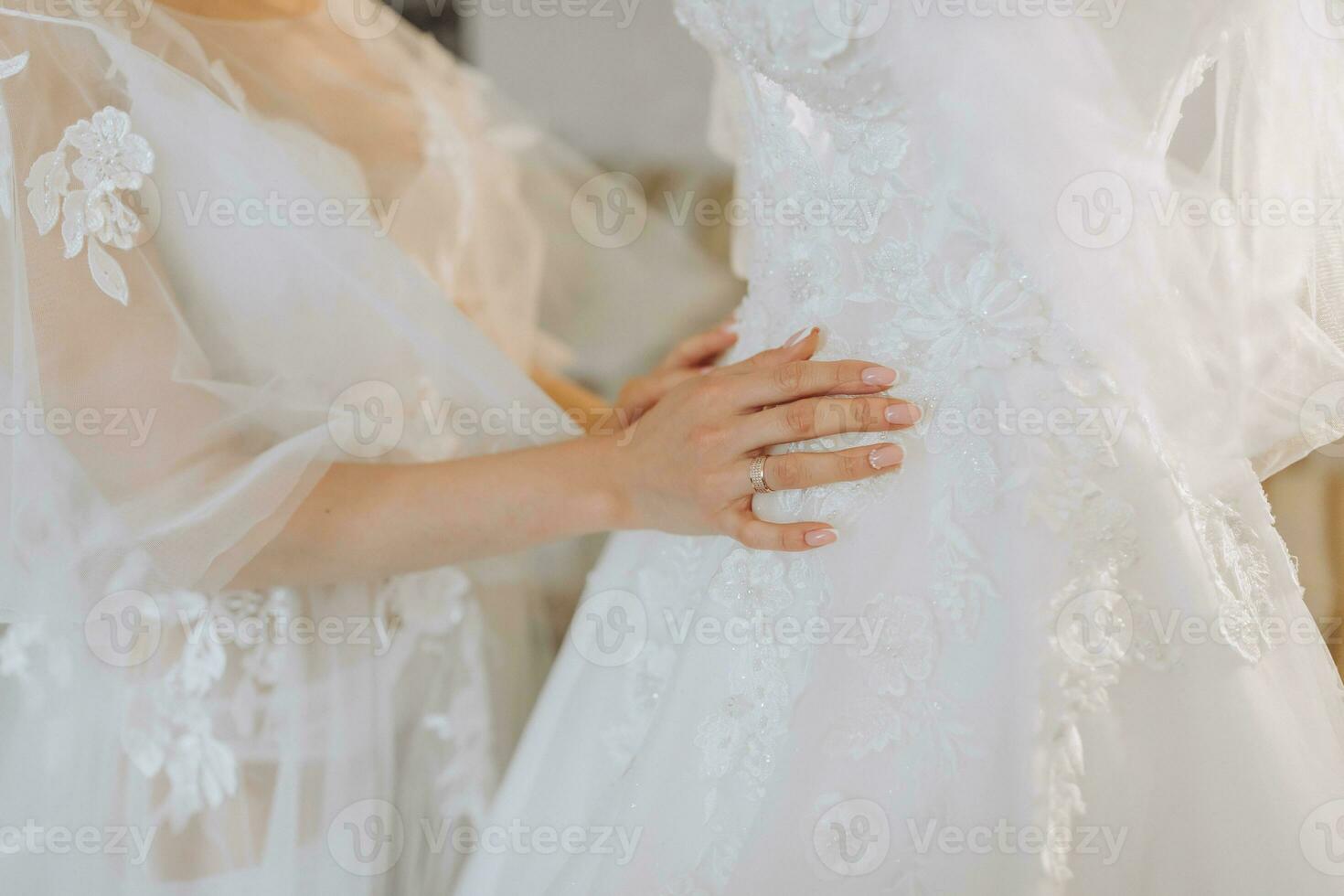 a beautiful girl with a wedding hairstyle in a transparent robe is preparing for a wedding in a hotel with a royal interior. The bride poses next to her wedding dress on a mannequin photo