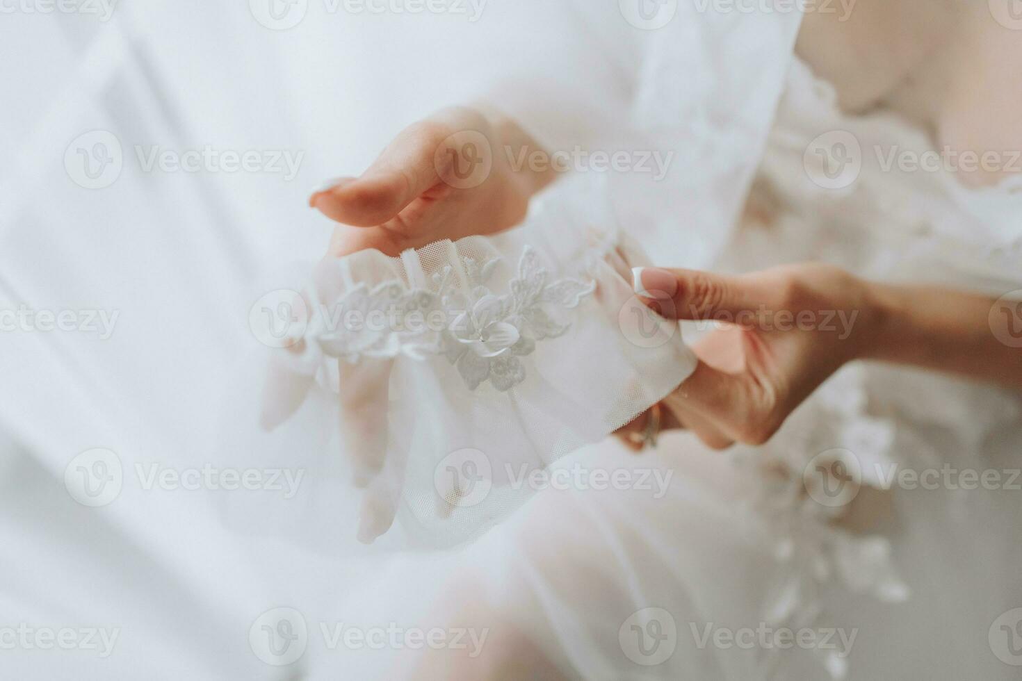 the bride with a French manicure holds a white garter in her hands. Close-up photo