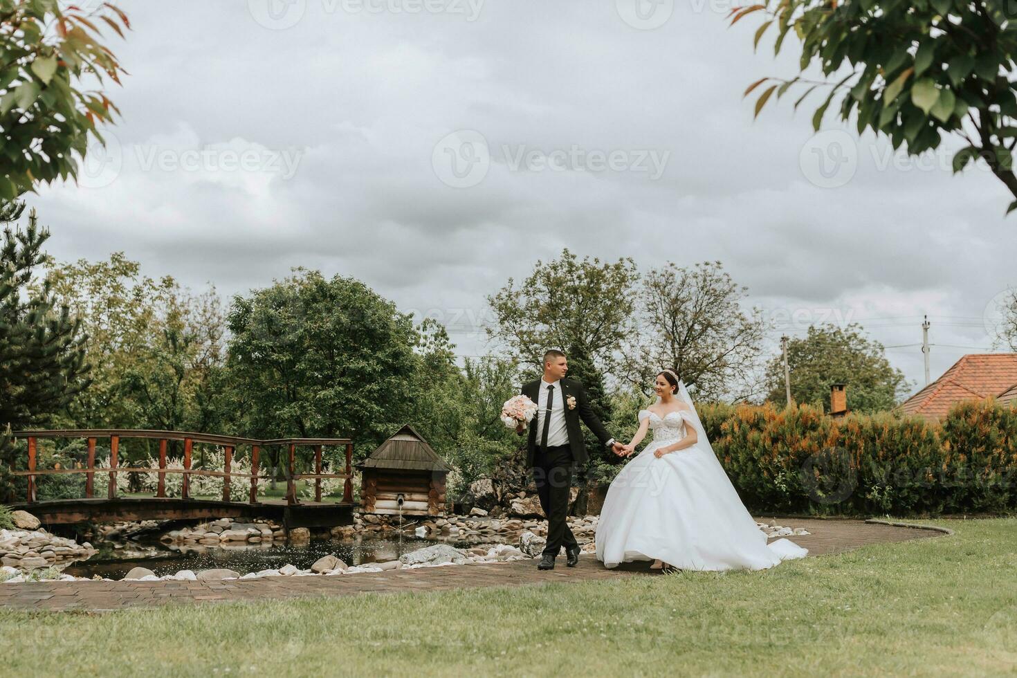 The bride and groom are walking and holding hands, looking at each other. Wide-angle photo in an overcast sky.