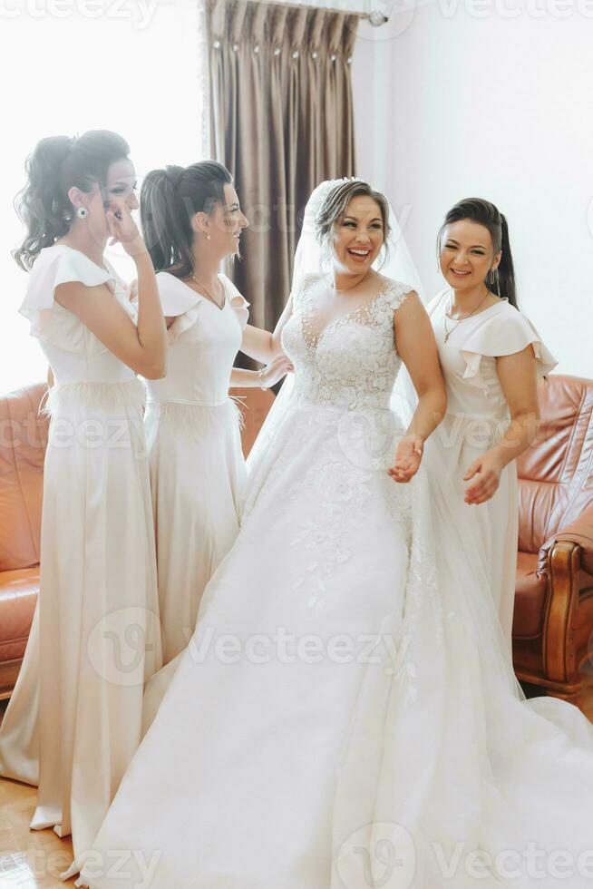 Wedding theme. The bride in a white dress, hugging her friend and posing together. Four brunettes. The last minutes of preparations for the wedding. The same outfit photo