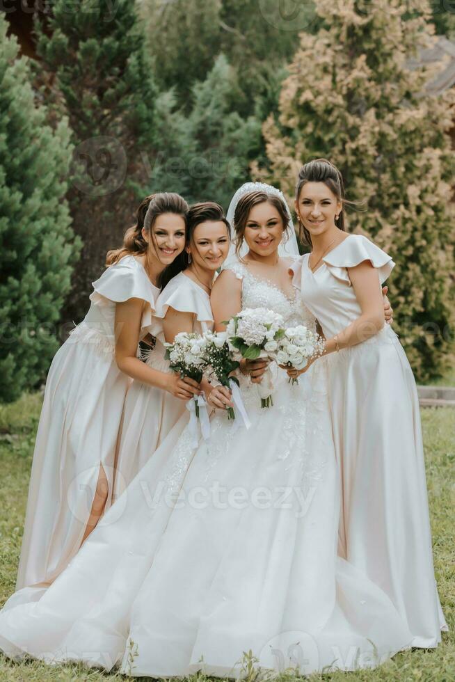 A group of beautiful girls with a bride in identical dresses are smiling, celebrating and having fun together against the background of nature and tall trees. Girls party photo