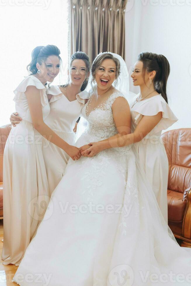 Wedding theme. The bride in a white dress, hugging her friend and posing together. Four brunettes. The last minutes of preparations for the wedding. The same outfit photo