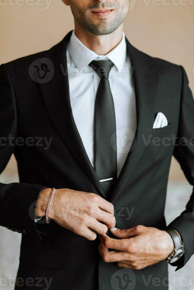 stylish man in a black classic suit with a tie. The groom is preparing for the wedding ceremony photo