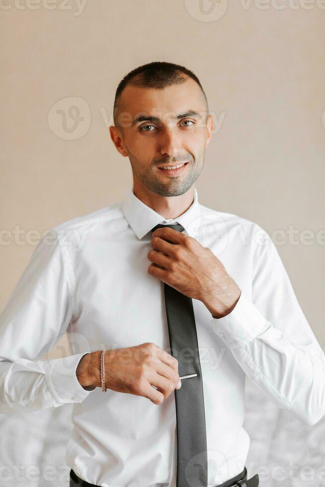 A man puts on a tie, a businessman prepares for a meeting. The groom is preparing for the ceremony photo