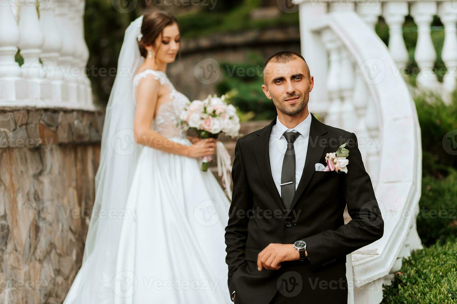 Portrait of a young bride in a white dress and a brunette groom in a suit on the stairs near the old city park. The man in the foreground. A beautiful and romantic wedding, a happy couple photo
