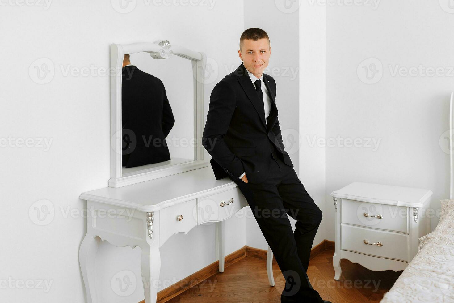 A stylish groom in a hotel room is dressed in a classic black suit. Groom's morning. The groom is getting ready in the morning before the wedding ceremony photo