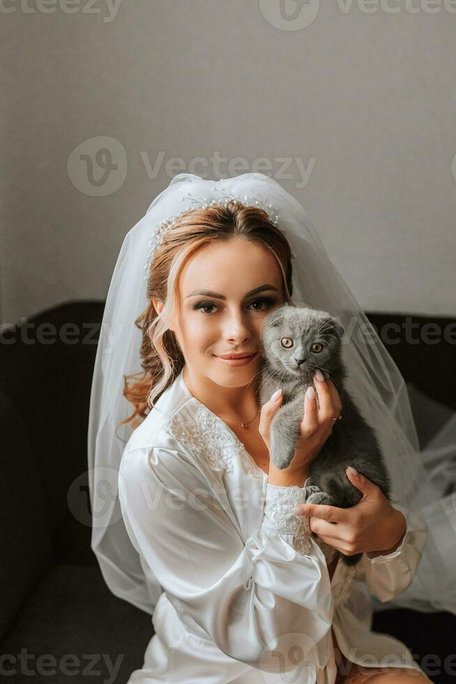 a young, elegant girl in the image of a bride with a beautiful veil on her head, holding her domestic cat in her arms Scottish Fold photo