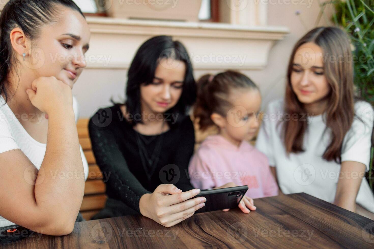 teenagers and one child having fun outdoors in a cafe. Friendship of children and teenagers. Four girls, dressed in different clothes, shout on the phone photo