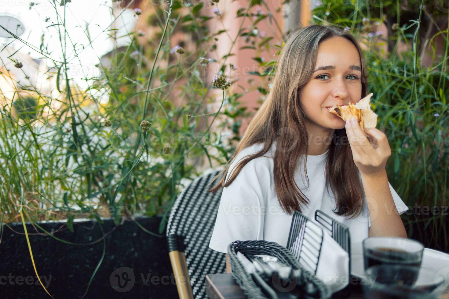 niña con largo pelo adolescente en un café comiendo pizza, al aire libre foto