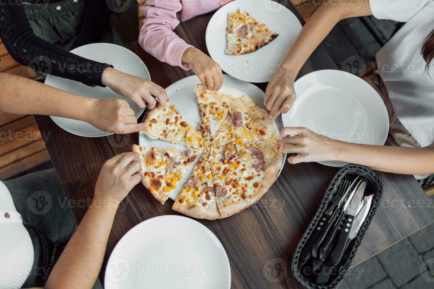 un gastos generales Disparo de un grupo de no identificado personas agarrando un rebanada de hawaiano Pizza foto