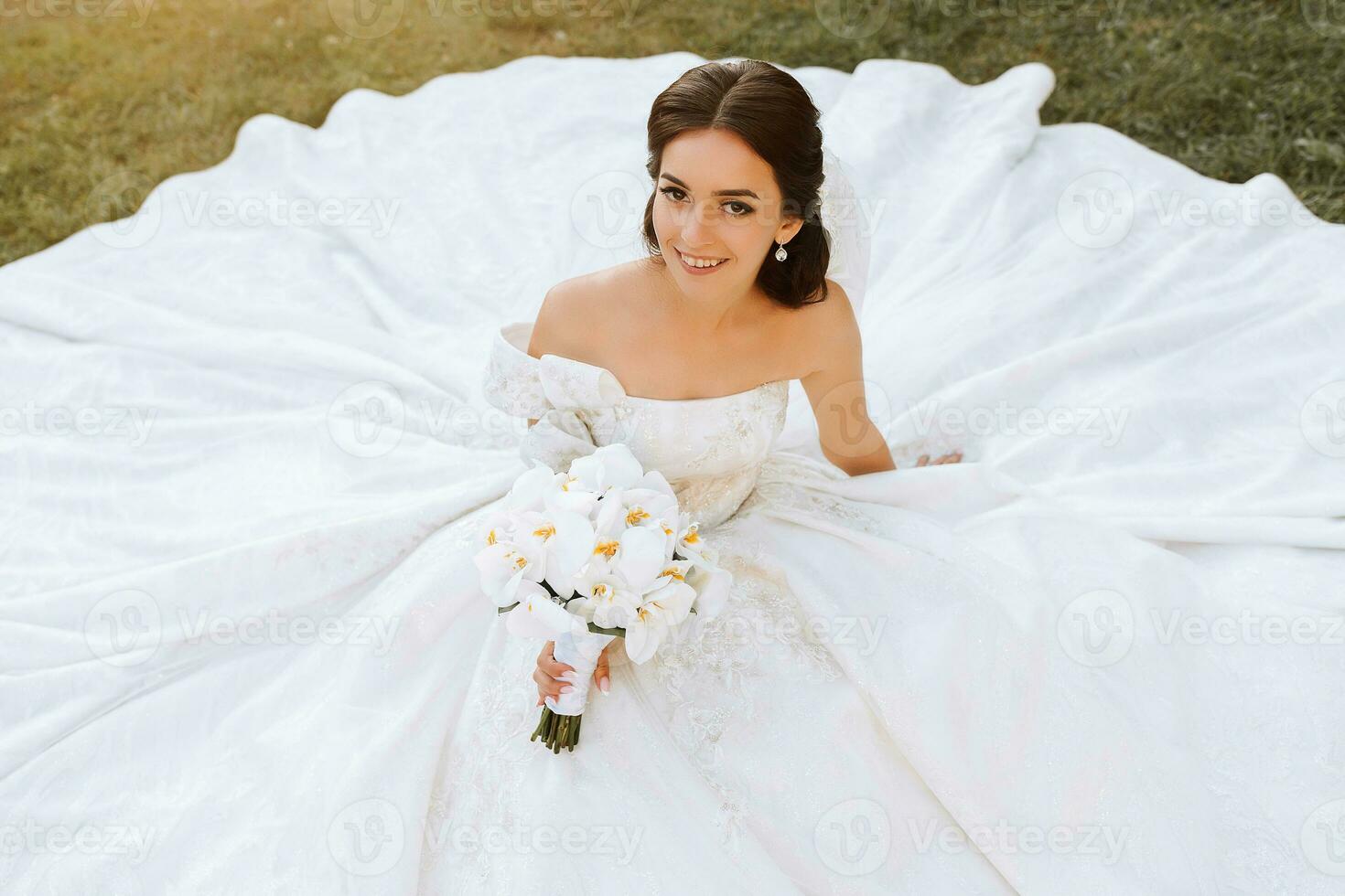 tender portrait of a happy bride with a bouquet of orchids in her hands, outdoors. Warm summer time. A long veil, a luxurious white dress with a train. photo