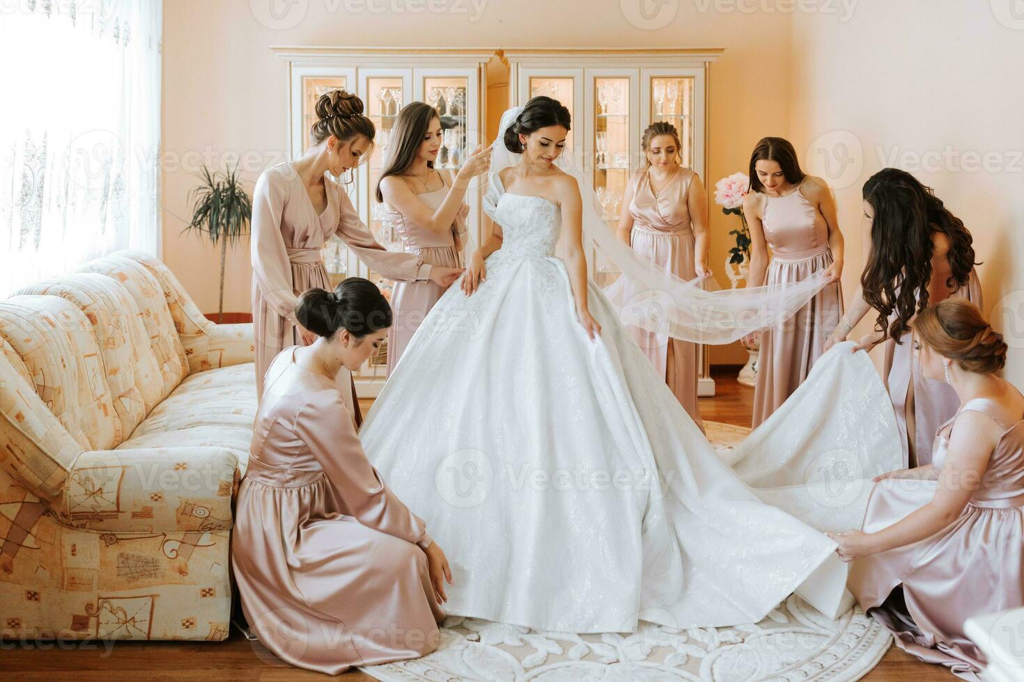 elegante hermosa damas de honor en pareo seda vestidos Ayudar maravilloso morena novia en blanco vestir obtener Listo para boda, Mañana preparativos, mujer poniendo en vestir foto