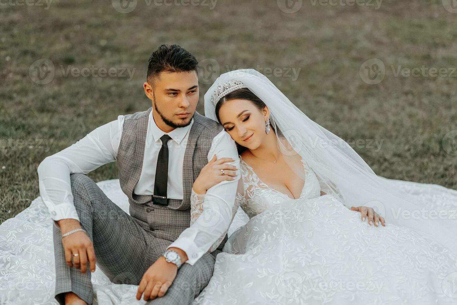 Fashionable groom and cute brunette bride in white dress with crown, hugging, laughing in park, garden, outdoors. Wedding photography, portrait of smiling newlyweds. photo