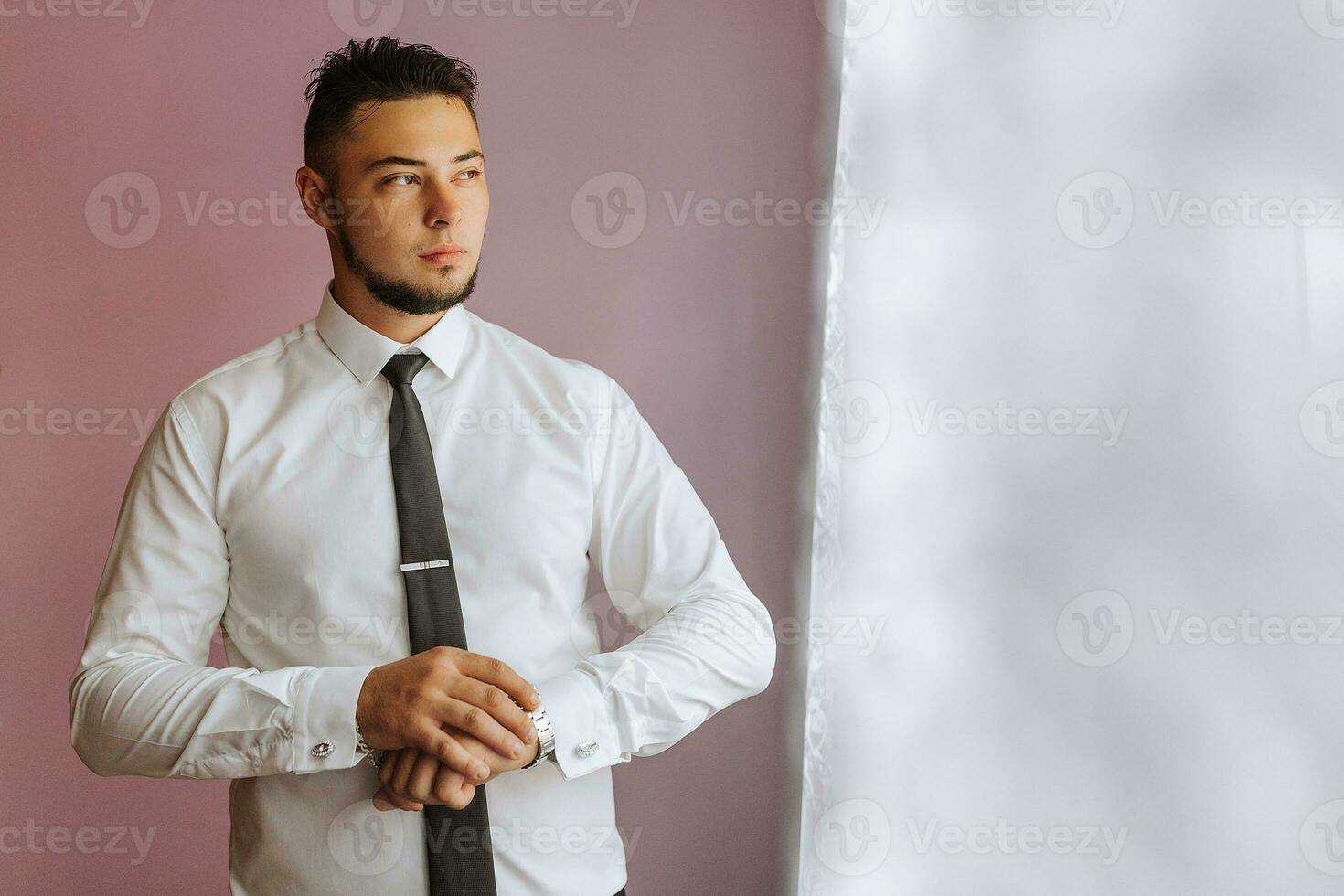 businessman dresses and adjusts his watch, preparing for a meeting. The groom is preparing for the wedding. The man wears a white shirt. Stylish groom photo