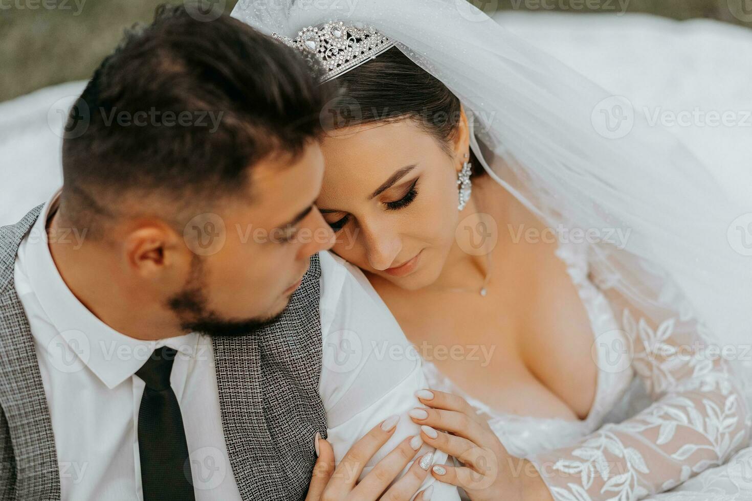 de moda novio y linda morena novia en blanco vestir con corona, abrazando, riendo en parque, jardín, al aire libre. Boda fotografía, retrato de sonriente recién casados. foto