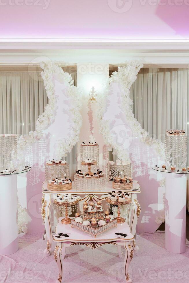 A delicious wedding. White cake decorated with flowers. Candy bar for a banquet. Celebration concept. Fashionable desserts. Table with sweets, candies. Fruits photo