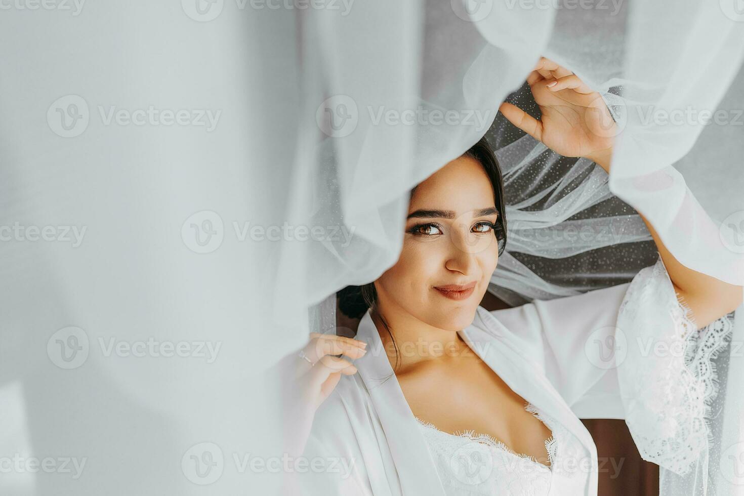 Portrait of a girl in a morning robe. Happy bride with professional make-up and long veil posing for photographer. The bride is preparing for the wedding photo