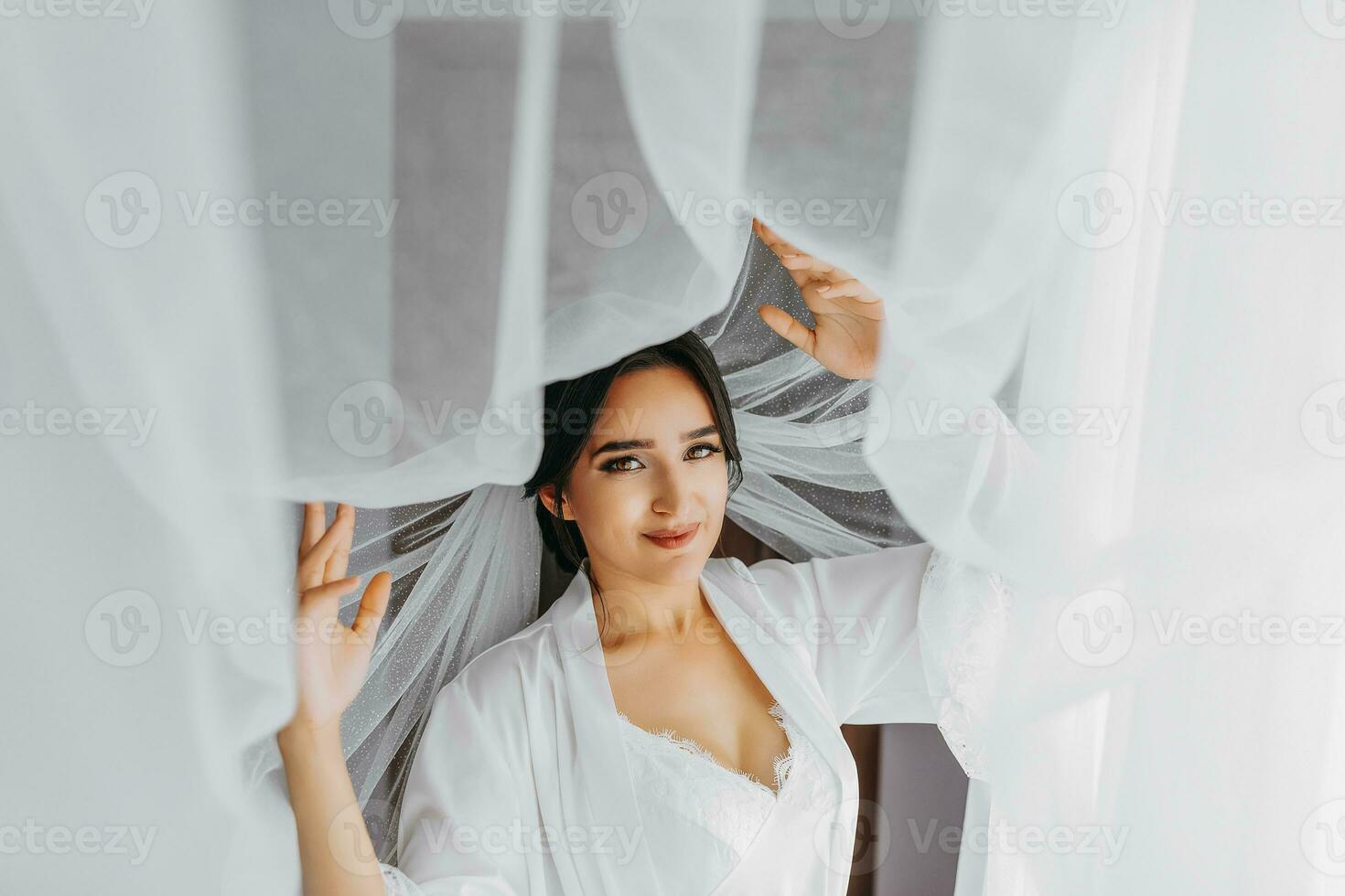 Portrait of a girl in a morning robe. Happy bride with professional make-up and long veil posing for photographer. The bride is preparing for the wedding photo