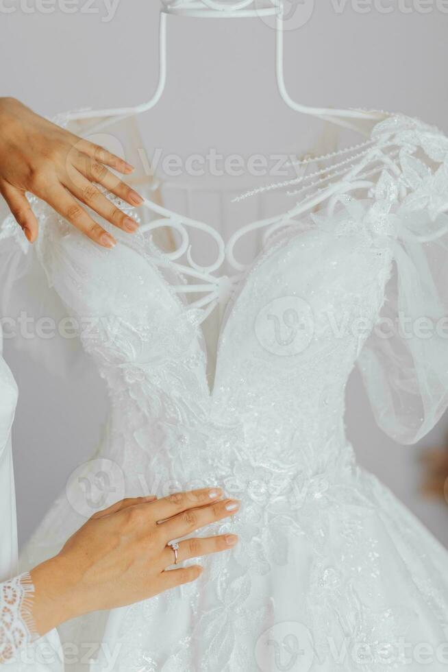 blanco Boda vestir con largo tren en habitación con hogar interior. el manos de el novia son en el vestir con un grande modelo foto