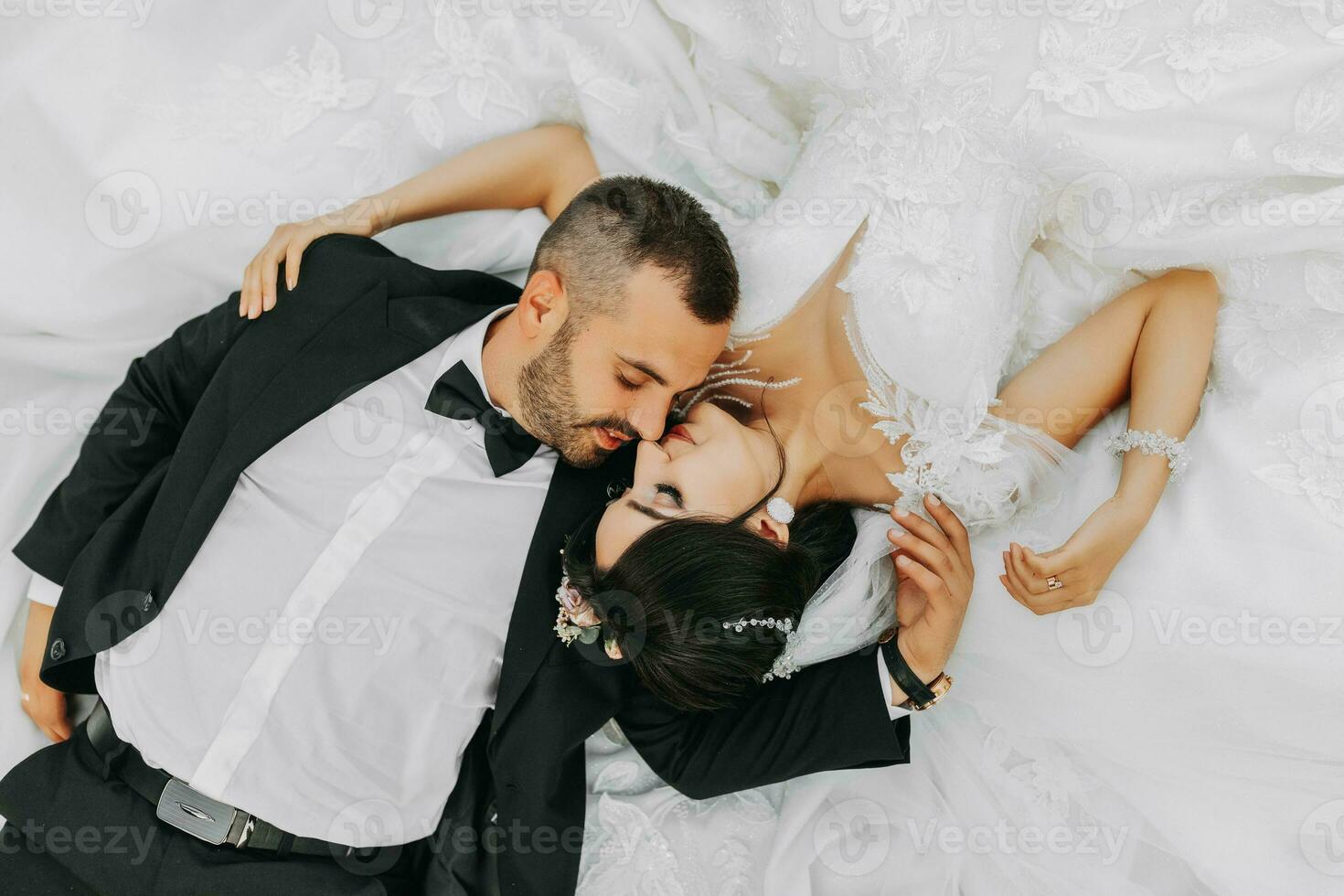 retrato de novia y novio acostado abajo y besando un increíblemente hermosa novia. elegante novio en un traje con un arco Corbata y un barba foto