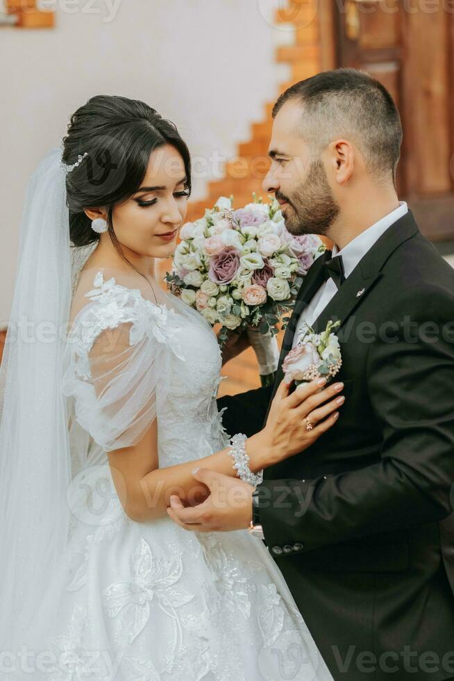 Portrait of a happy newlywed wife and husband hugging outdoors and enjoying a wedding bouquet of white roses. Sincere feelings of two young people. The concept of true love. photo