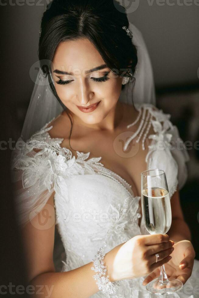 lujo mujer vistiendo blanco vestir participación vaso de champán en luz de sol. Boda concepto. profesional maquillaje y cabello. contento novia foto