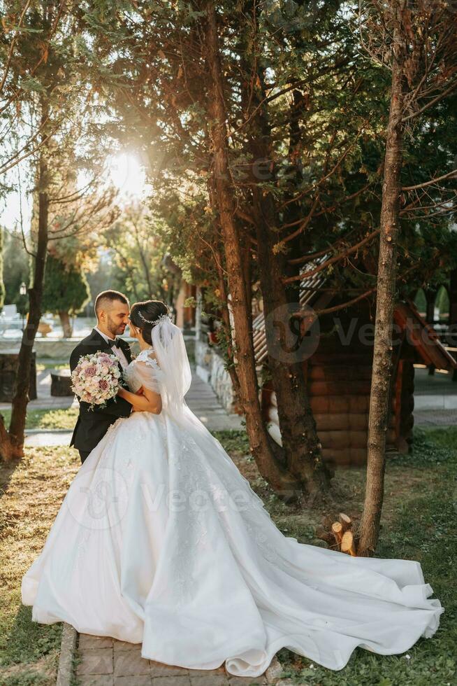 un hermosa novia en un de moda Boda vestir y el novio son abrazando en el parque a puesta de sol. un maravilloso joven novia es increíblemente contento. contento niña en su Boda día foto