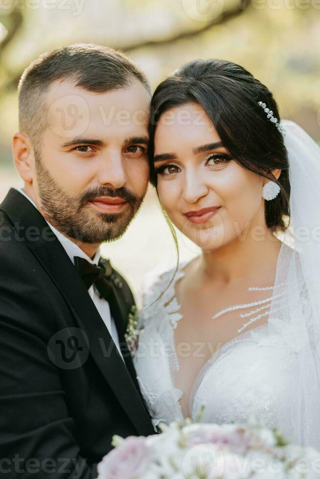 Portrait of a happy newlywed wife and husband hugging outdoors and enjoying a wedding bouquet of white roses. Sincere feelings of two young people. The concept of true love. photo