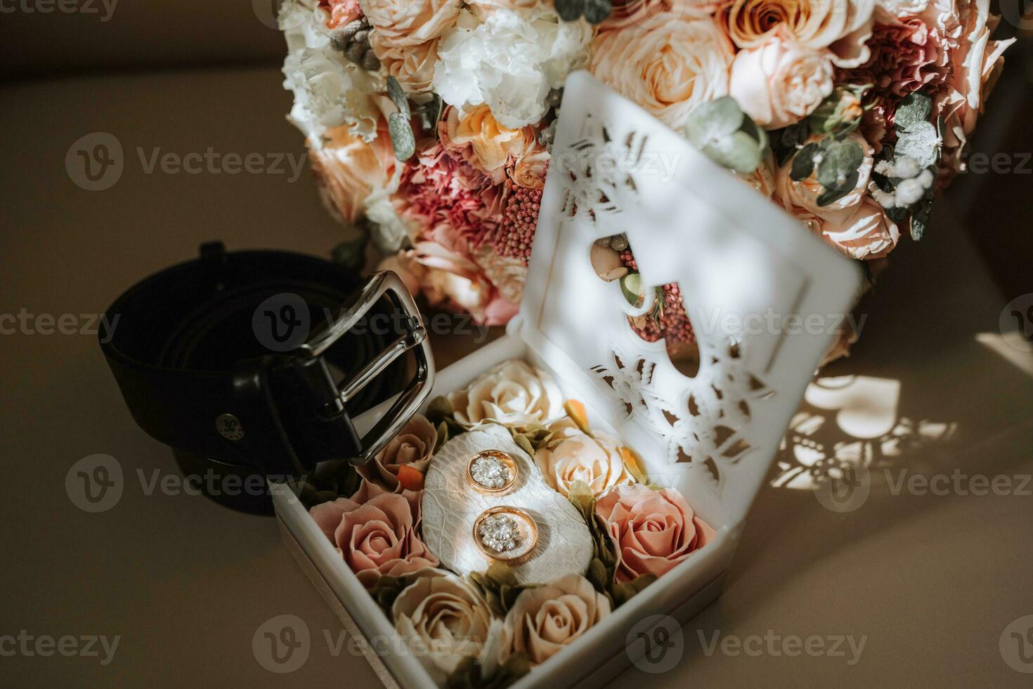 Gold wedding rings in a box decorated with flowers. Black men's belt. Details of the groom photo