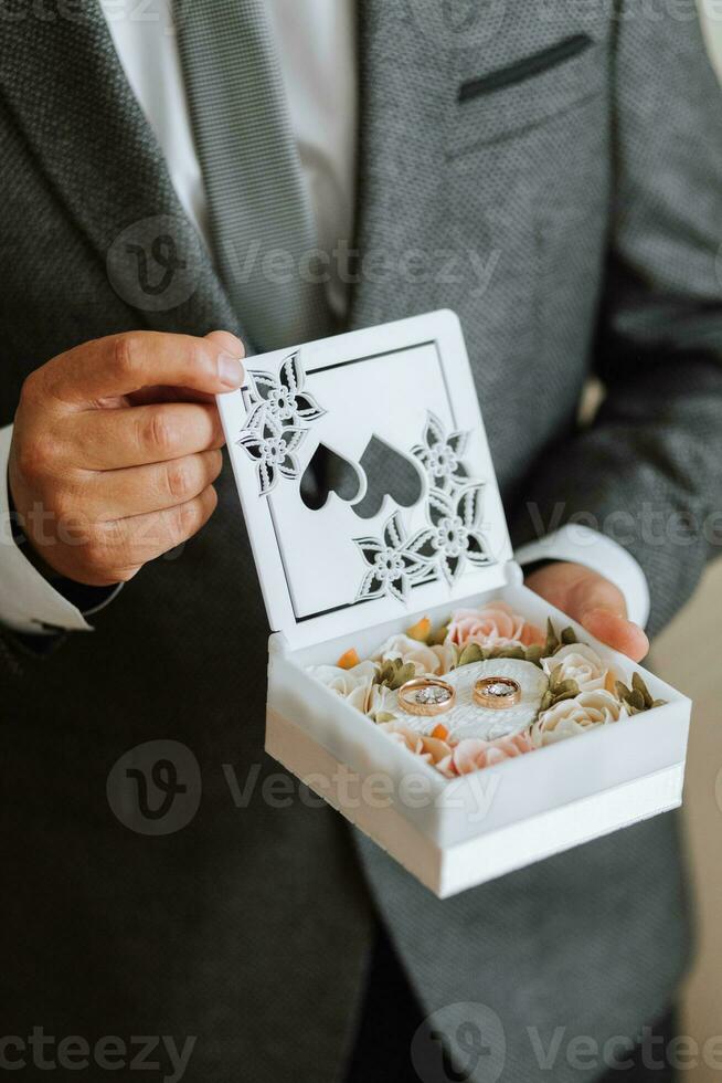 Gold wedding rings in a box decorated with flowers in the hands of the groom close-up photo