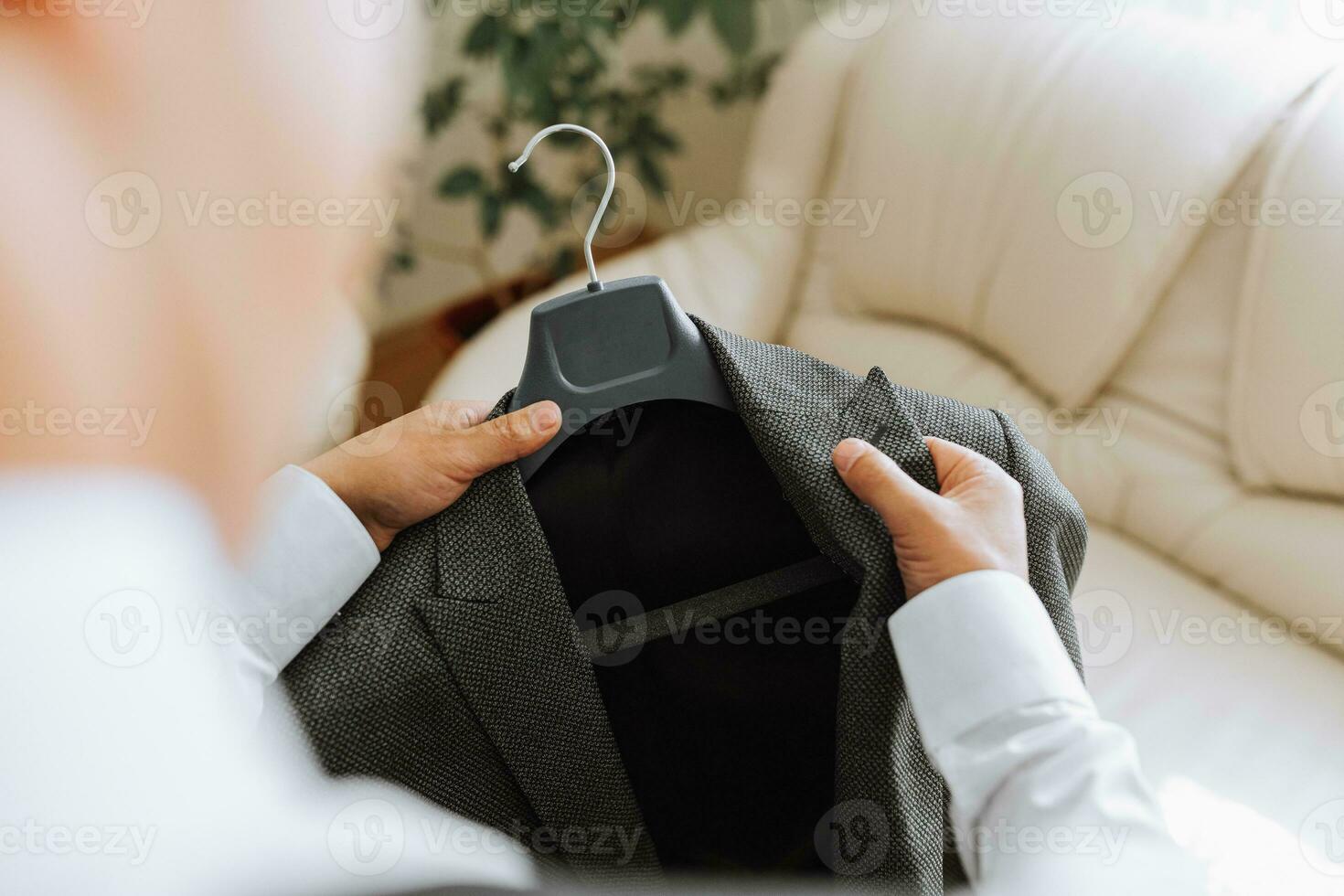 el hombre sostiene su negro chaqueta en un percha en su manos. el novio es preparando para el Boda ceremonia. detallado de cerca foto de manos