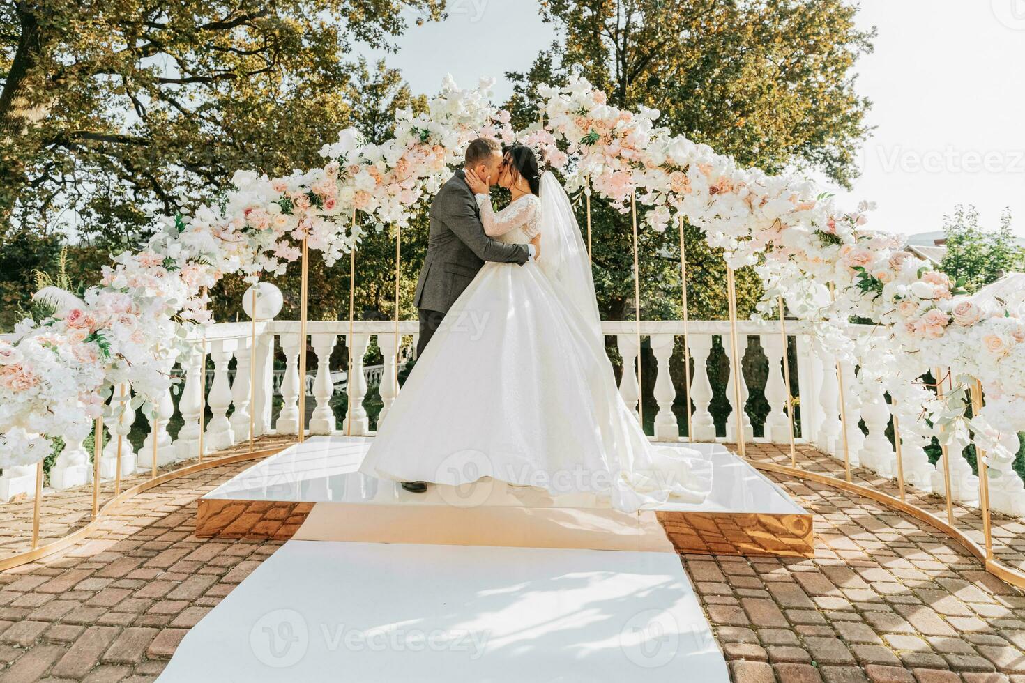 happy bride and groom kissing at the wedding ceremony. The wedding arch is decorated with rose flowers photo