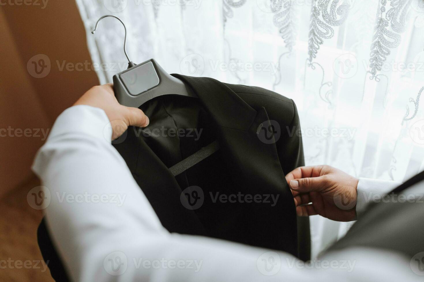 el hombre sostiene su negro chaqueta en un percha en su manos. el novio es preparando para el Boda ceremonia. detallado de cerca foto de manos