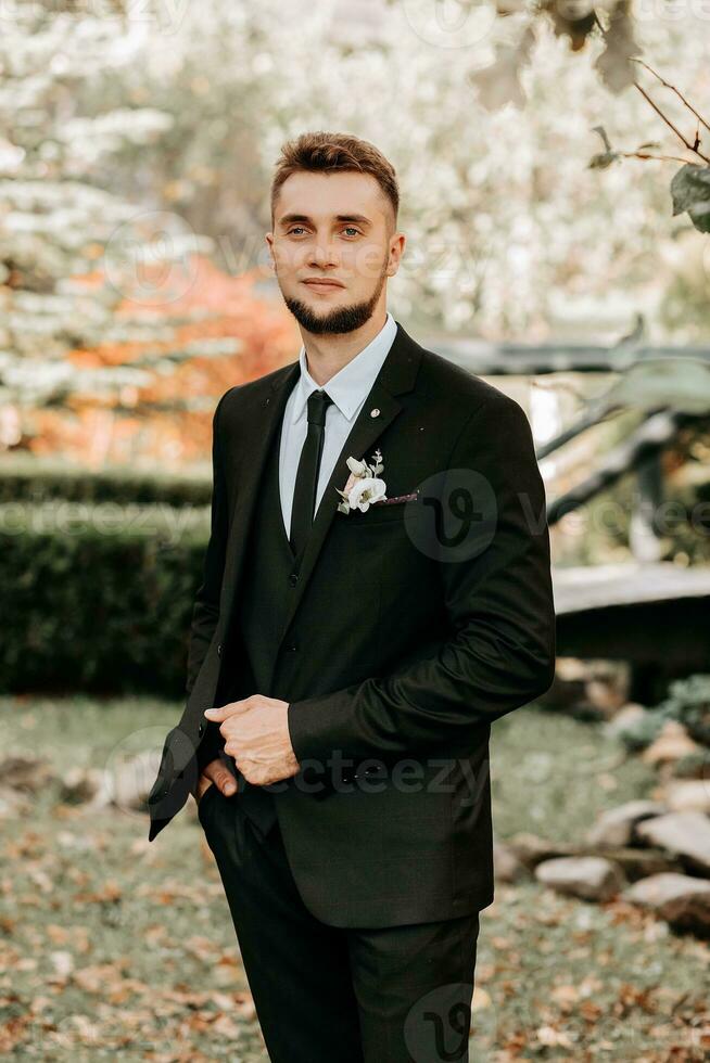 portrait of the groom in a black suit with a beard, looking into the lens photo